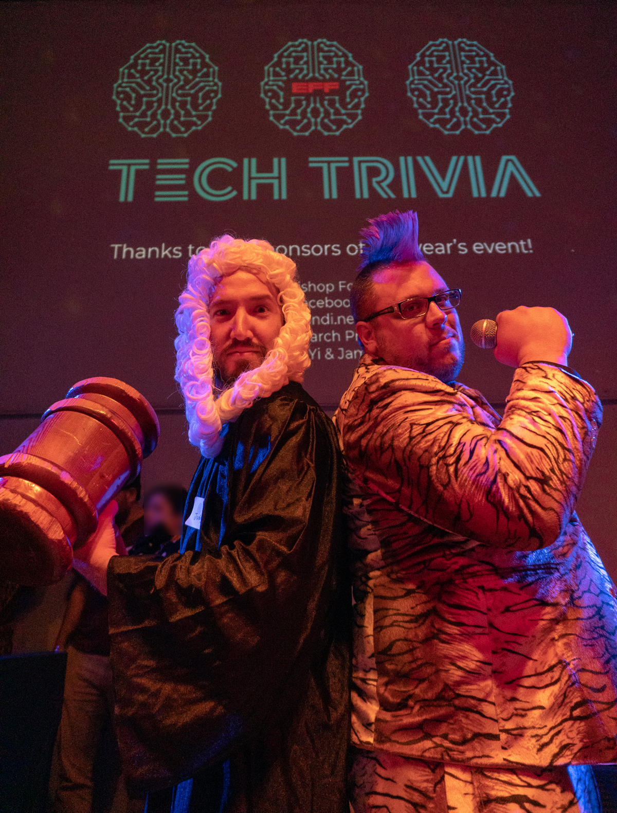 Did we mention that A man holding an oversized gavel, wearing a parliamentary wig, with his back against a man with a mohawk wearing a tiger striped suit and holding a microphone.